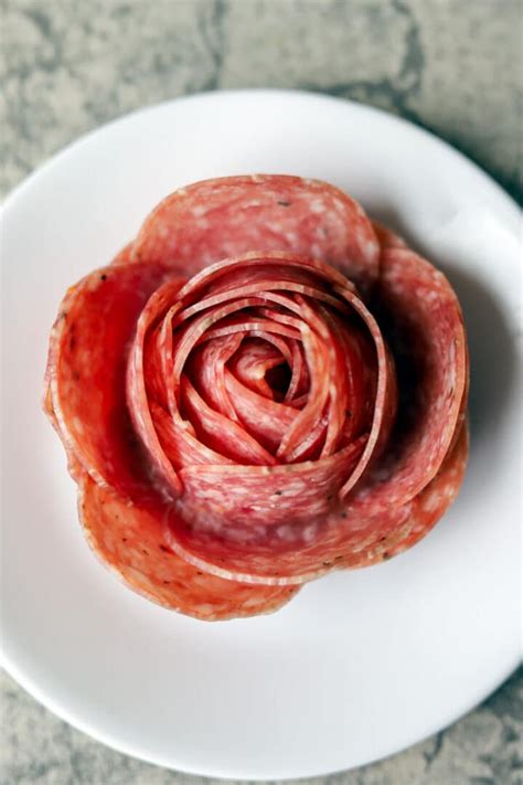 Form the Salami Roses. To make the roses, you'll need 4 large pieces of salami for each rose. Place the salami on top of each other, staggering them so that about a half inch is showing for the bottom layers. Once you have them in line, fold them in half. Starting at one end, begin tightly rolling to form the rose.